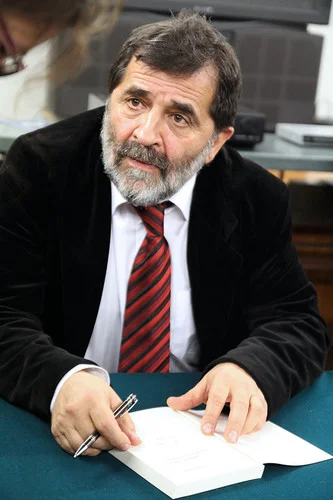 A man in a suit and tie with burgundy and black stripes, listening carefully, focused
